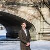 Honoree Alex Cagle wearing a long winter coat and standing next to a bridge