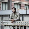 30 Under 30 honoree Landry Bado smiling and leaning on a metal scaffolding