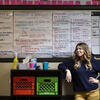 30 under 30 honoree Michelle Ferguson Shore leaning on storage boxes in front of a whiteboard displaying lesson plans and a calendar